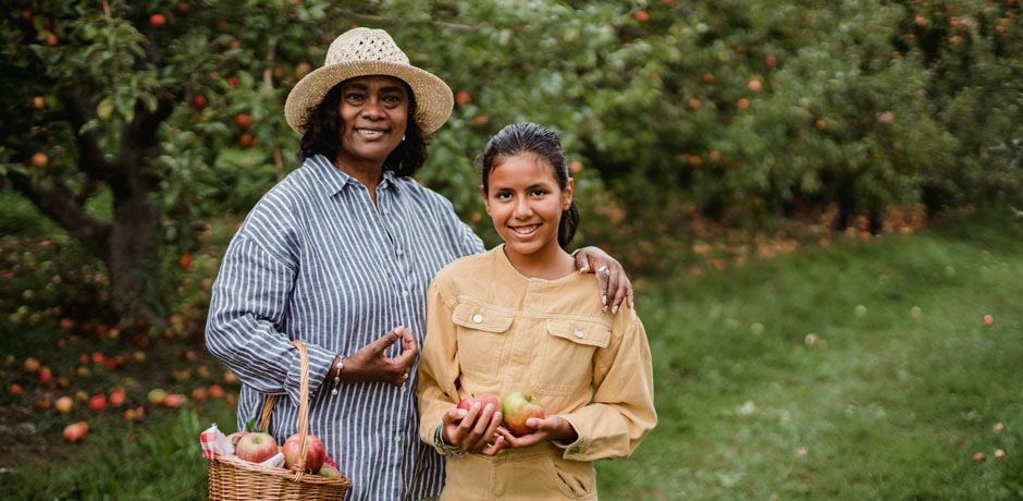 Penny Juice Family. Older woman and younger girl picking fresh apples, healthy ingredients used in Penny Juice Concentrates.