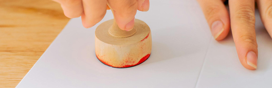 A round stamp being pressed onto a piece of paper on a table.